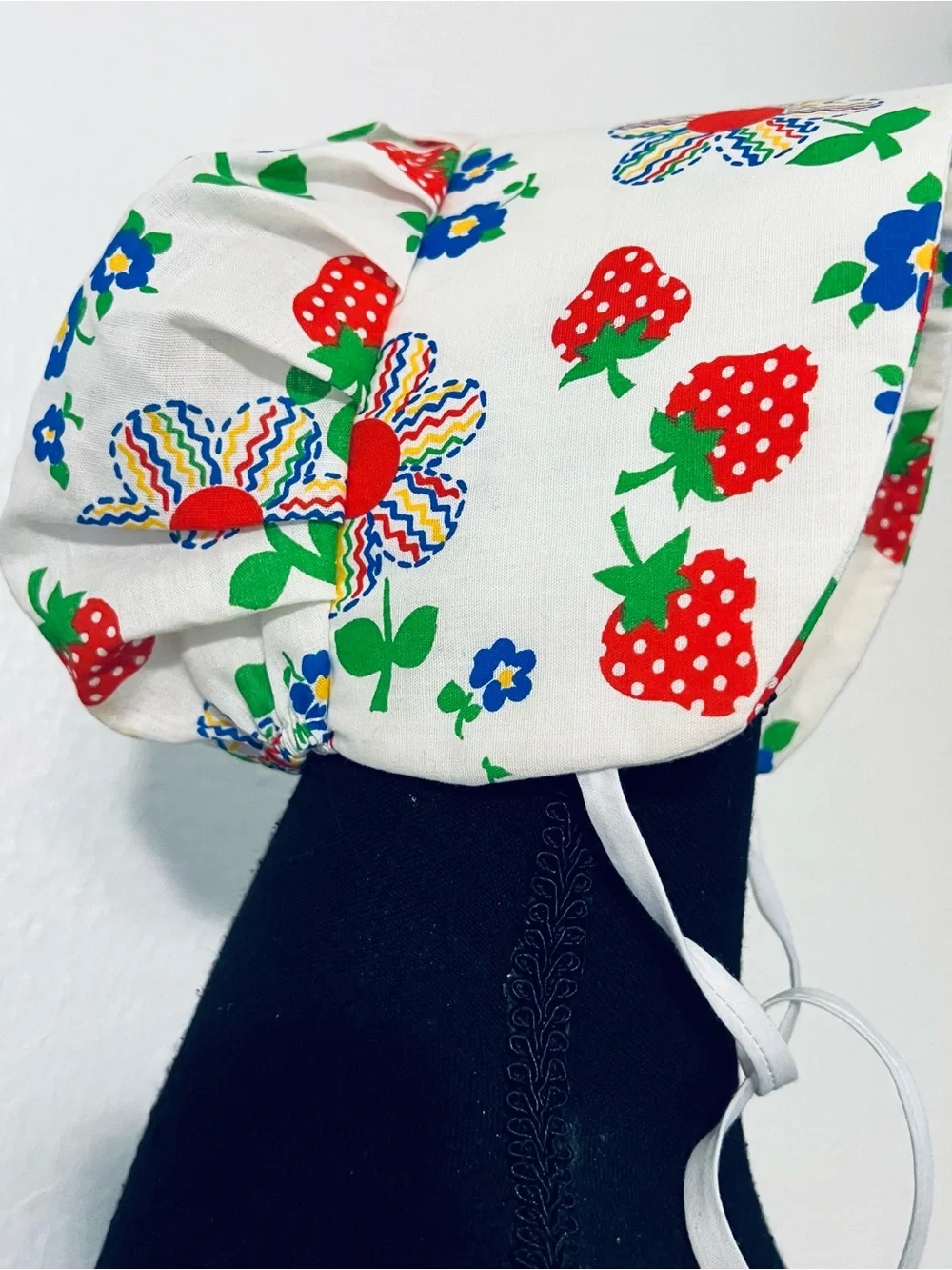 Charming vintage-style baby sunbonnet features a playful white fabric patterned
